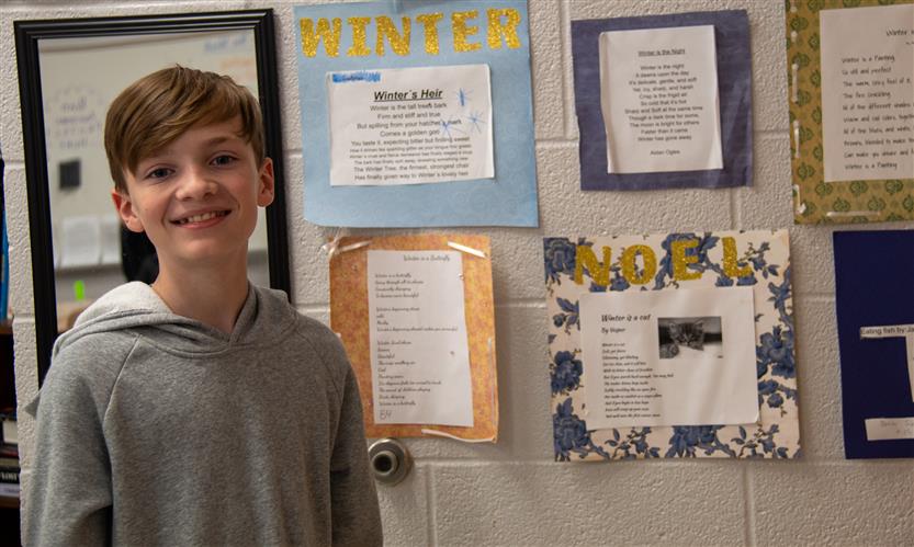 A boy smiles while standing in a school hallway